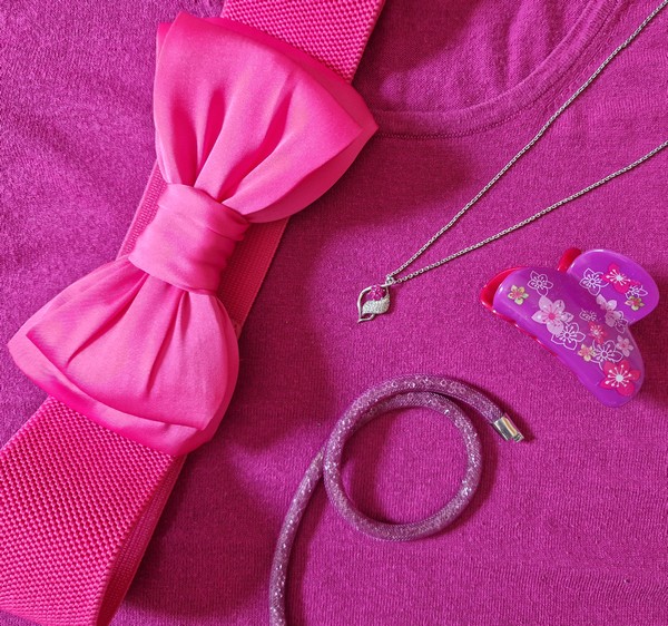 Abbildung verschiedener pinkfarbener Accessoires - eine Kette, Haarklemme, Gürtel - auf einem pinkfarbenen Untergrund